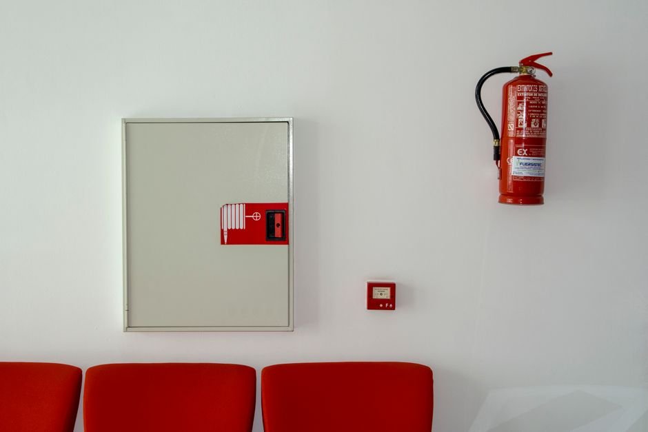 Extintor y equipo de seguridad montados en una pared blanca con un asiento rojo debajo.
