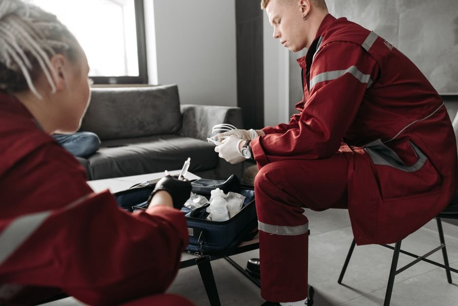 Paramédicos con uniformes rojos atienden a una emergencia médica en interiores, preparando equipos médicos.